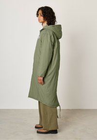 Zielona parka z kapturem o długim, luźnym fasonie, wykonana z lekkiego materiału. Posiada boczne zamki błyskawiczne oraz prostą grafikę na piersi.