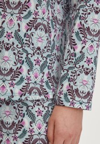 Katoenen pyjama set met een blauwe achtergrond en ingewikkelde bloemmotieven in donker bordeaux, roze en teal, met zichtbare stiksels.