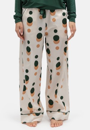 Loszittende crèmekleurige broek met grote donkergroene en beige stippen, gedragen door een persoon die op blote voeten staat.