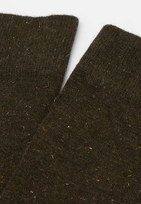 Ciemnozielone skarpetki wykonane z teksturowanego materiału z metalowymi złotymi nitkami, z prążkowanym brzegiem i miękkim, dziewiarskim wyglądem.