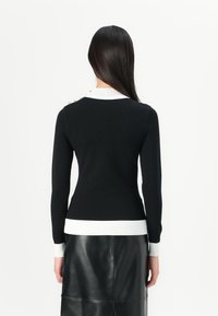 Zwarte trui met een witte kraag en manchetten, slim fit, lange mouwen en gouden knoopaccenten op de schouder.