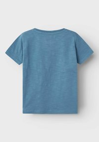 Camiseta de manga corta con cuello redondo en un tejido azul claro con un efecto jaspeado. Textura suave con un diseño simple, sin patrones ni acentos.