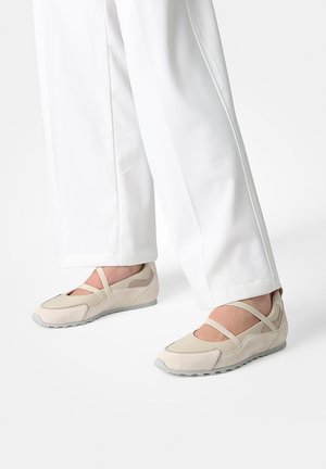 Beige, multifunktionale Schuhe mit einem Obermaterial aus Wildleder, mit gekreuzten Riemen und Gummisohlen, kombiniert mit weißen, locker sitzenden Hosen.
