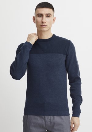 Granatowy sweter o fakturze z gładką, jednolitą wstawką na ramionach. Żebrowane mankiety i dół, okrągły dekolt, dopasowany krój. Dyskretne logo na dole.