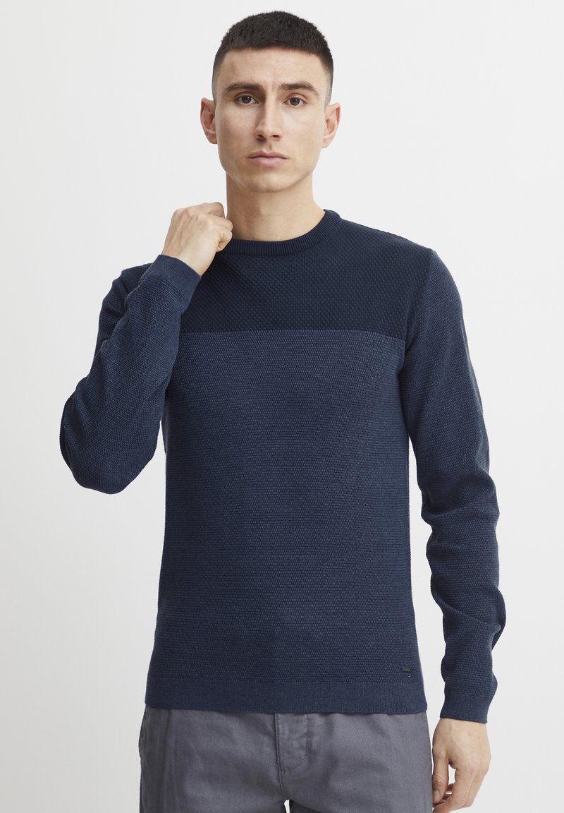 Granatowy sweter o fakturze z gładką, jednolitą wstawką na ramionach. Żebrowane mankiety i dół, okrągły dekolt, dopasowany krój. Dyskretne logo na dole.