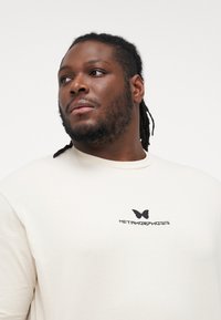 Cream-colored t-shirt made from soft fabric, featuring a black butterfly graphic and the word "METAMORPHOSIS" in bold black text.