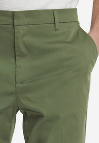 Olivgröna skräddarsydda byxor med en slät yta, utrustade med sidofickor och en slim fit-design, tillverkade av ett lätt tyg.