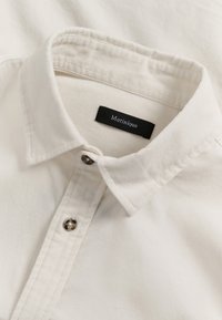 Camicia bianca con un tessuto testurizzato, con bottoni frontali e una piccola etichetta nera con il nome del marchio "Matinique."