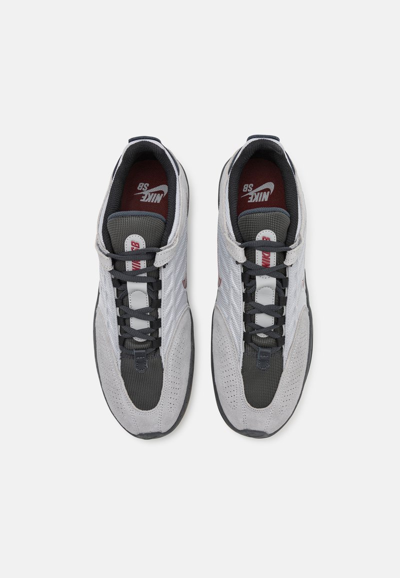 Graue und schwarze Sneaker mit einem Obermaterial aus Mesh und Wildleder, ausgestattet mit einem Schnürdesign, gepolstertem Kragen und roten sowie weißen Akzenten auf der Zunge.