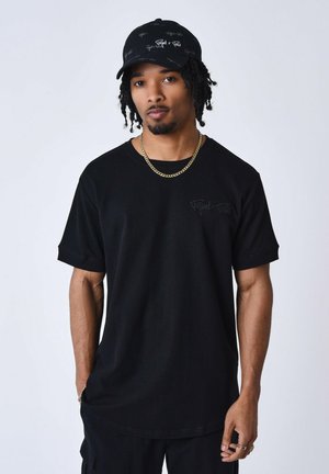 Camiseta negra de manga corta, textura acanalada, con un pequeño logotipo blanco en el pecho. Combinada con una gorra negra a juego.
