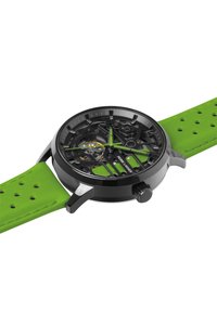 Reloj con esfera negra esqueleto y acentos verdes, con una correa de goma. Presenta una caja metálica, correa perforada y movimiento visible.