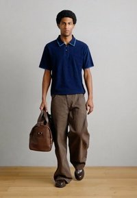 Μπλε ναυτικό πόλο με υφασμένο γιακά, συνδυασμένο με χαλαρά καφέ παντελόνια. Κρατώντας καφέ δερμάτινη τσάντα, συμπληρώνοντας με σκούρα παπούτσια.