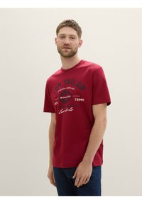 Rød bomulds t-shirt med rund hals, korte ærmer og grafisk print på fronten, der indeholder tekst og designelementer.