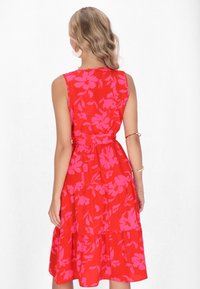 Ärmelloses rotes Kleid mit pinkem Blumenmuster, gestuftem Design und Gürtel-Detail in der Taille. Glattes Material und knielanger Saum.
