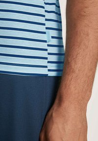 Blue and light blue striped t-shirt with a tag displayed, paired with dark blue fabric below. The texture appears smooth and soft.