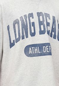 Γκρι φούτερ με μεγάλο μπλε κείμενο "LONG BEACH" και μικρότερο κείμενο "ATHL. DEPT" τυπωμένο στο μπροστινό μέρος.