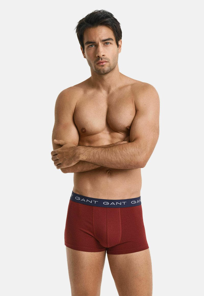 Bordeauxrote Boxershorts mit einem marineblauen Bündchen, das mit dem wiederholten "GANT"-Logo versehen ist. Der Stoff ist glatt und das Design sitzt eng an.
