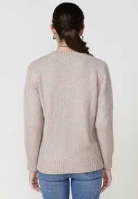 Suéter de punto beige con un corte holgado, que presenta una superficie texturizada y un sutil brillo. Los puños y el dobladillo acanalados añaden detalle al diseño.