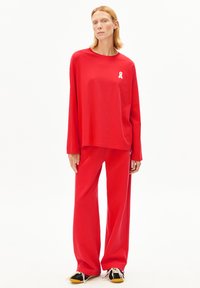 Rode top met lange mouwen met een wit lintlogo en bijpassende broek met wijde pijpen. De stof lijkt zacht met een gladde structuur en een losse pasvorm.