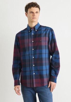 Plaid shirt in blue, burgundy, and black, featuring a button-down collar, long sleeves, and a curved hem. Textured cotton fabric.