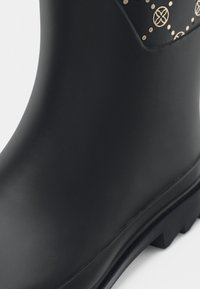 Botte en caoutchouc noir à finition lisse, avec un accent à motif près du haut et une semelle rainurée pour une meilleure traction.