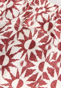 Gros plan sur un tissu blanc avec des motifs de soleil rouge rouille et une poche cousue, avec une ceinture élastique en haut.