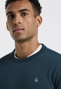 Marineblauwe sweatshirt met een geribbelde ronde hals, voorzien van een witte binnenkraag en een geborduurd pinguïnlogo op de linkerborst.