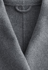 Pilkas vilnonis paltas su švelnia tekstūra, turintis giliai V formos iškirptę, matomus siūlus ir apvalų kilpą prie apykaklės.