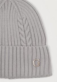 Pelēka adīta cepure ar ribotu tekstūru un kabeli adījuma dizainu. Priekšā ir metālisks "G" logotipa akcentu.