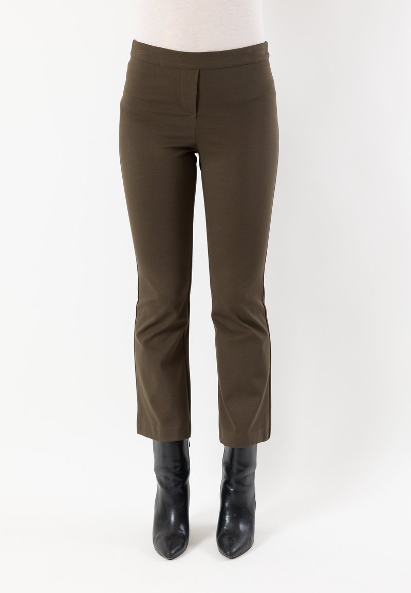 Pantaloni marroni elasticizzati con vita aderente e gamba affusolata, abbinati a stivaletti neri con punta affilata su uno sfondo semplice.