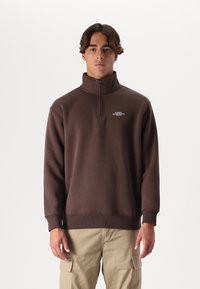 Brown zip-up sweatshirt made of soft fabric, featuring a high collar and ribbed cuffs, with a small logo on the chest area.