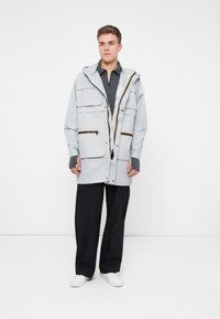 Heled hall kapuutsiga jakk mitme taskuga, lukuga ja mustade aktsentidega. Kandub tumeda särk üle ja sobitub mustade pükste ning valgete kingadega.