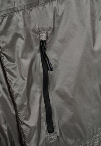 Zbliżenie na szare nylonowe tkaniny z pionowym czarnym zamkiem błyskawicznym wyposażonym w dwa suwaki i wzmocnione przeszycia wokół obszaru zamka.