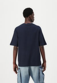 Tricou de culoare bleumarin, cu mânecă scurtă și guler rotund, fabricat din bumbac, având o tăietură lejeră și detalii subtile de cusătură la tiv.