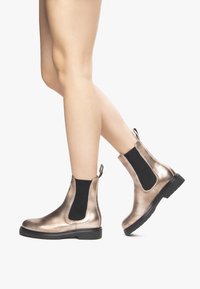 Bottines Chelsea en bronze métallique avec des panneaux élastiques sur les côtés, en cuir texturé et semelles en caoutchouc noir, dotées de languettes à l'arrière.