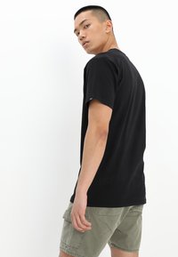 Svart kortärmad t-shirt i bomull. Ryggsidan är enkel med en avslappnad passform. Bärs tillsammans med ljusgröna cargoshorts med sidofickor.