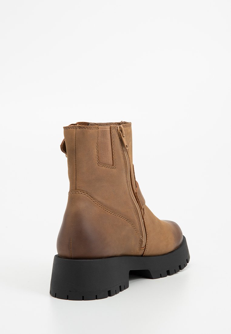 Botín de cuero marrón hasta el tobillo con acabado texturizado, cierre de cremallera y suela negra gruesa con profundas ranuras para mayor tracción.