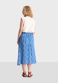 Jupe midi à motif bleu avec une silhouette évasée, associée à un haut sans manches crème et des sandales à lanières marron.