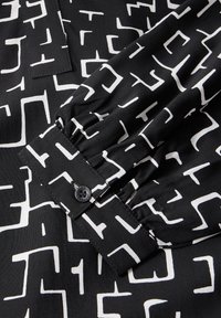 Svart tyg med ett vitt geometriskt mönster, med en samlad ärmslut och en kontrasterande knapp, som återspeglar en slät textur.