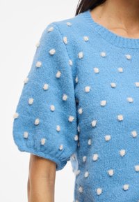 Suéter de color azul claro con mangas cortas abullonadas, con puntos blancos en relieve, hecho de un suave tejido de punto texturizado.