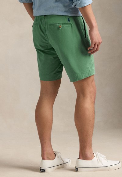 Zaļas kokvilnas šorti ar piegulošu dizainu, aizmugurējā kabata ar pogas aizdari un izšūtu logotipa detaļu. Kombinēti ar baltām sporta kurpēm.