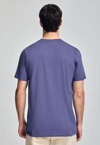 Lila t-shirt i bomull med rund halsringning och korta ärmar, med en jämn yta och rak fåll. Inga synliga mönster eller detaljer.