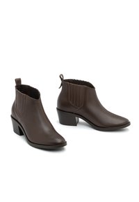 Brązowe skórzane botki za kostkę z ostrym noskiem i słupkowym obcasem. Posiadają elastyczne boczne panele i uchwyt do łatwego zakładania. Gładka faktura.