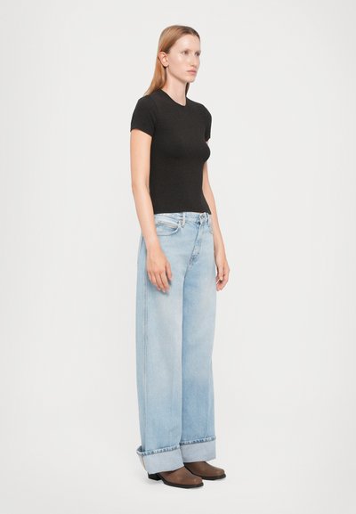 Black fitted T-shirt paired with light blue wide-leg jeans, featuring a cuffed hem and a faded texture. Model standing against a white background.
