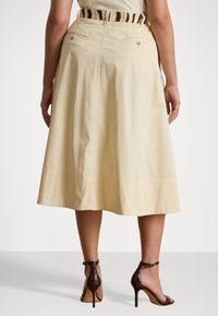 Una gonna di cotone beige chiaro, lunga fino al ginocchio, caratterizzata da un design semplice, tasche posteriori e una cintura a strisce coordinata con una texture leggera.
