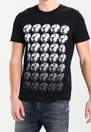 Homme portant un t-shirt noir avec plusieurs motifs de globe blancs en rangées, un globe a un texte rouge "DIESEL" en haut à droite.