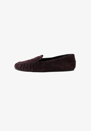 Mocassino in camoscio marrone scuro con suola piatta, cuciture in stile mocassino e dettaglio con cinturino sulla parte superiore.