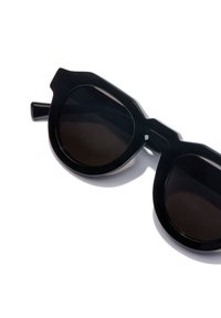 Schwarze Sonnenbrille mit einem auffälligen, kantigen Design, ausgestattet mit großen, dunklen Gläsern und kräftigen Kunststoffrahmen. Akzentuiert mit einem verlängerten Bügeldesign.