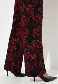 Zwarte stoffen broek met een gestructureerd ontwerp en rode rozenpatronen, gecombineerd met zwarte stilettohakken.