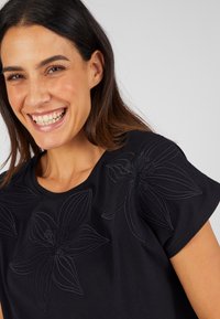 Zwarte top met korte mouwen, voorzien van textuurrijke bloemenborduursels in een tonale uitvoering over de voorkant. Zachte stof en een relaxte pasvorm.